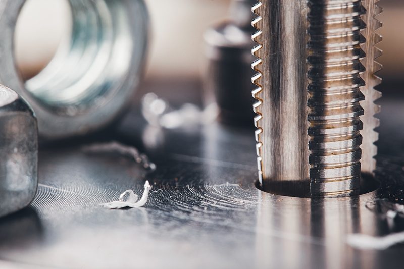 Gewinde_schneiden Detailaufnahme von einem Gewindeschneider mit Spänen auf einer Metalloberfläche.