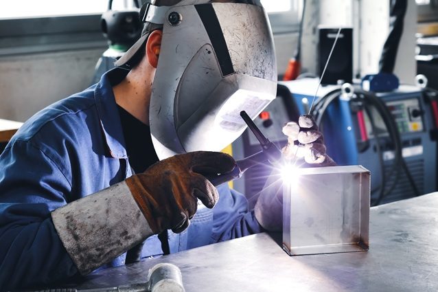 WIG_Schweißen Ein Mensch schweißt an einem Metallblock in einer Werkstatt.